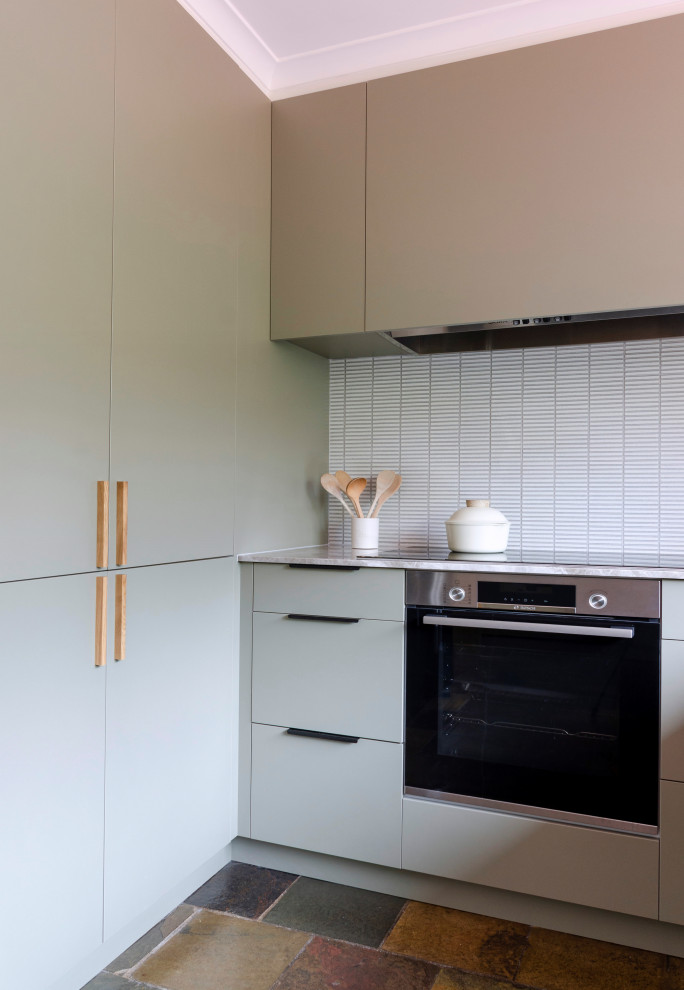 Design ideas for a mid-sized midcentury u-shaped kitchen pantry in Melbourne with a single-bowl sink, flat-panel cabinets, green cabinets, limestone benchtops, white splashback, mosaic tile splashback, black appliances, slate floors, a peninsula, brown floor and beige benchtop.