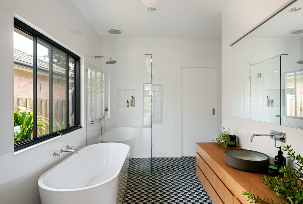 Contemporary master bathroom in Melbourne with flat-panel cabinets, medium wood cabinets, a freestanding tub, a corner shower, white tile, white walls, a vessel sink, wood benchtops, grey floor, a hinged shower door, brown benchtops, a single vanity and a floating vanity.