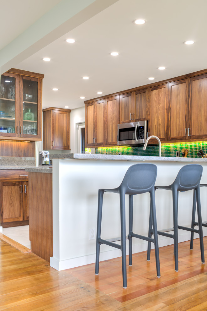 Photo of a mid-sized transitional l-shaped eat-in kitchen in Hawaii with medium wood cabinets, granite benchtops, green splashback, mosaic tile splashback, stainless steel appliances, porcelain floors, no island, an undermount sink and shaker cabinets.