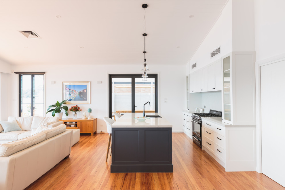 Design ideas for a transitional galley open plan kitchen in Newcastle - Maitland with a drop-in sink, shaker cabinets, white cabinets, black appliances, medium hardwood floors, with island, brown floor and grey benchtop.