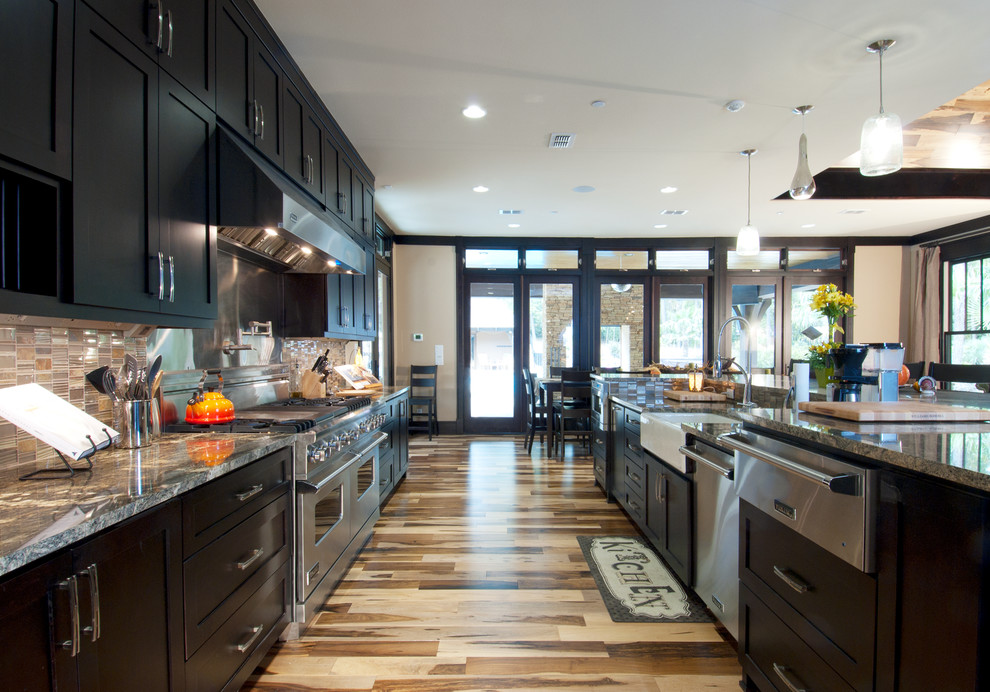 Inspiration for an arts and crafts galley eat-in kitchen in Dallas with a farmhouse sink, shaker cabinets, dark wood cabinets, granite benchtops, multi-coloured splashback, glass sheet splashback, stainless steel appliances, light hardwood floors and with island.