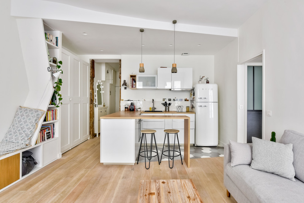 This is an example of a mid-sized scandinavian u-shaped open plan kitchen in Paris with a drop-in sink, flat-panel cabinets, white cabinets, wood benchtops, white splashback, porcelain floors, a peninsula, grey floor and beige benchtop.