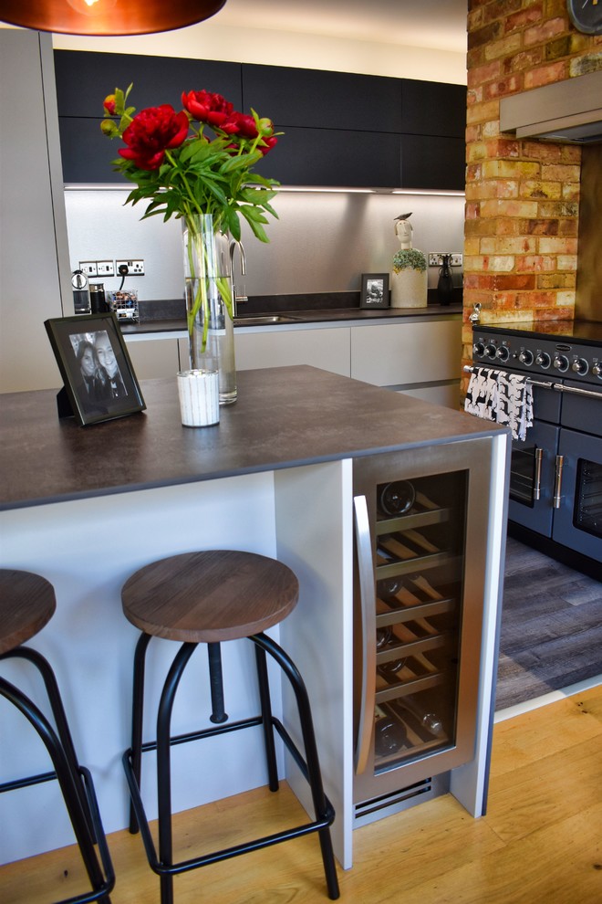 Inspiration for a large contemporary kitchen/diner in Cambridgeshire with a submerged sink, flat-panel cabinets, beige cabinets, black appliances, light hardwood flooring, an island and grey worktops.