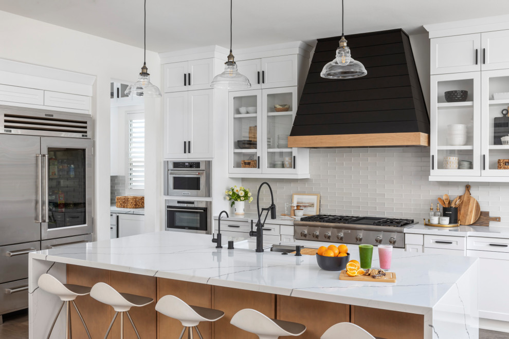 Inspiration for a small modern galley open plan kitchen in Orange County with a farmhouse sink, shaker cabinets, white cabinets, quartzite benchtops, white splashback, glass tile splashback, stainless steel appliances, dark hardwood floors, with island, brown floor and white benchtop.