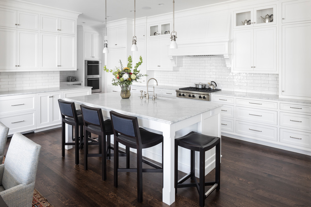 Inspiration for a beach style l-shaped eat-in kitchen in Minneapolis with an undermount sink, shaker cabinets, white cabinets, white splashback, dark hardwood floors, with island, brown floor and white benchtop.