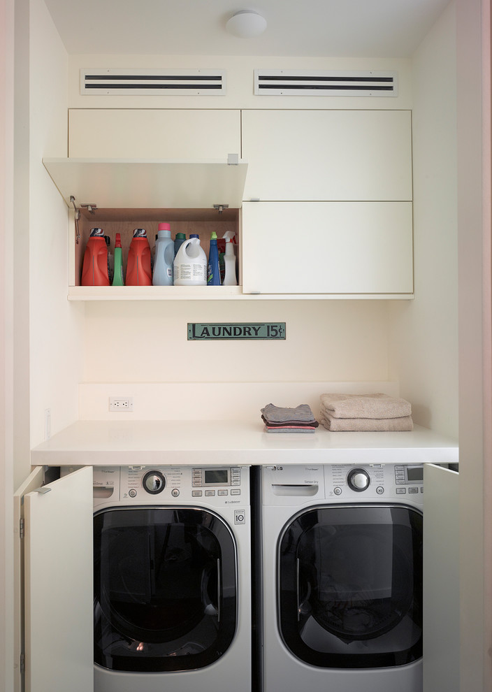 Small modern single-wall laundry cupboard in San Francisco with flat-panel cabinets, solid surface benchtops, beige walls, white cabinets and a concealed washer and dryer.