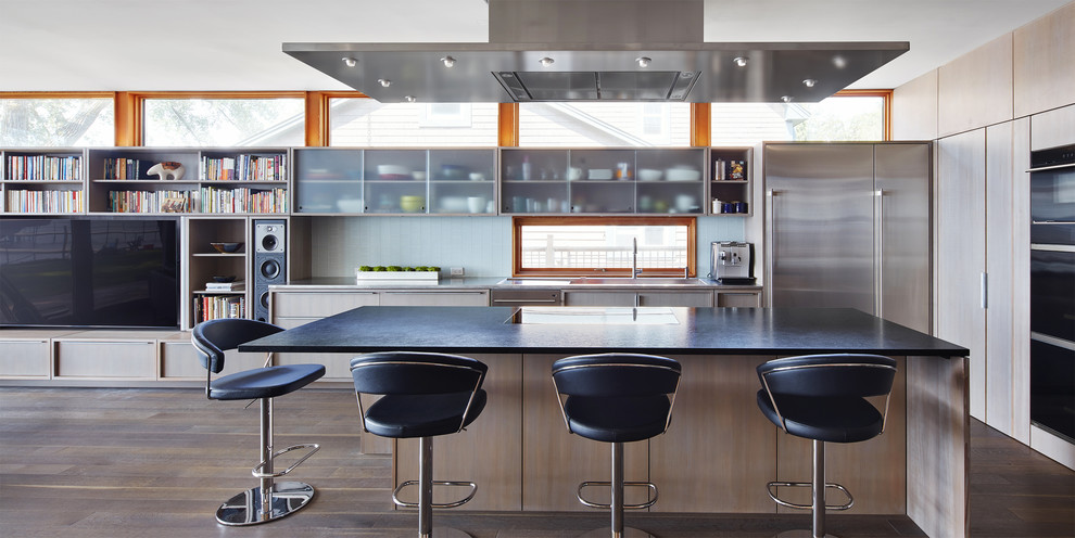 Photo of a small contemporary l-shaped open plan kitchen in Minneapolis with an undermount sink, glass-front cabinets, granite benchtops, blue splashback, glass tile splashback, stainless steel appliances, dark hardwood floors, with island, brown floor, black benchtop and light wood cabinets.