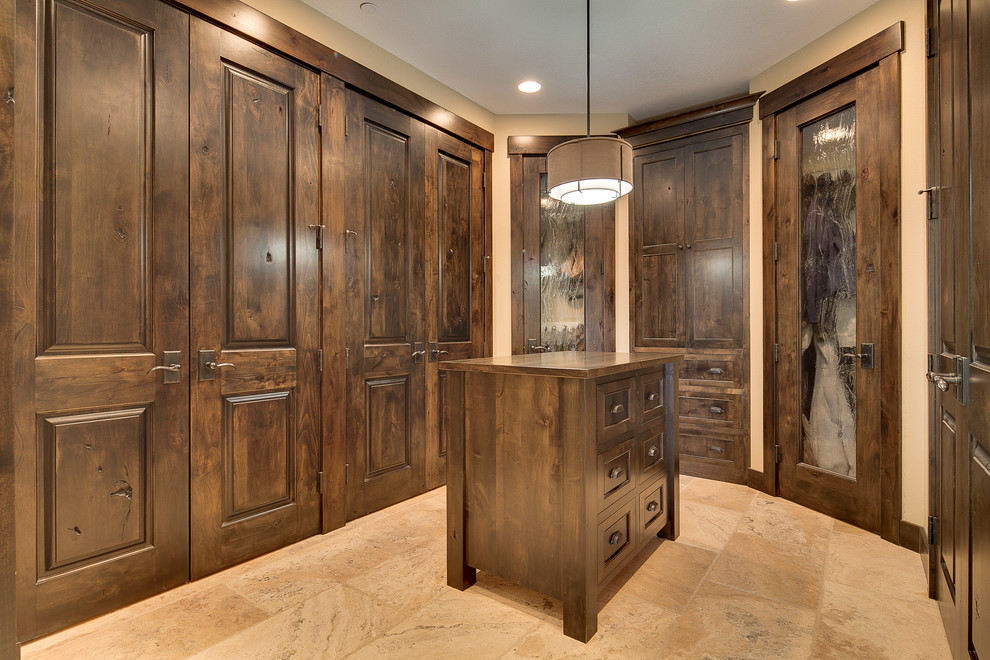 Photo of a large country gender-neutral walk-in wardrobe in Portland with dark wood cabinets and travertine floors.