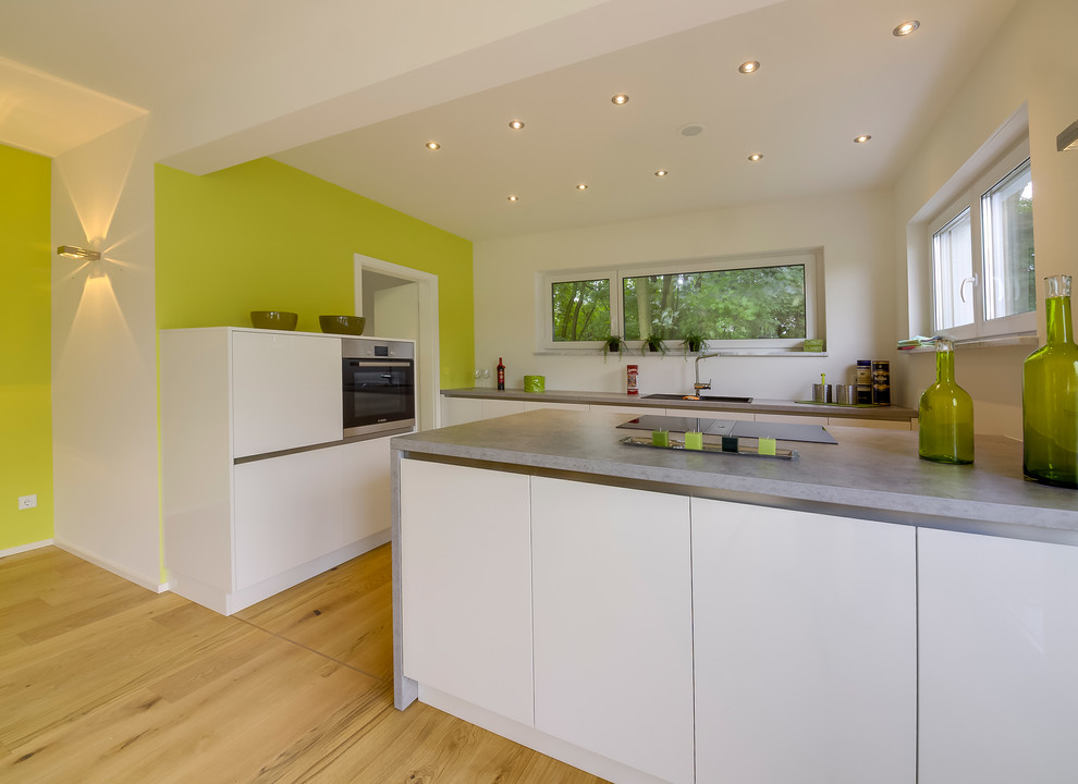This is an example of a large contemporary open plan kitchen in Other with a drop-in sink, flat-panel cabinets, white cabinets, medium hardwood floors, a peninsula, granite benchtops and white splashback.