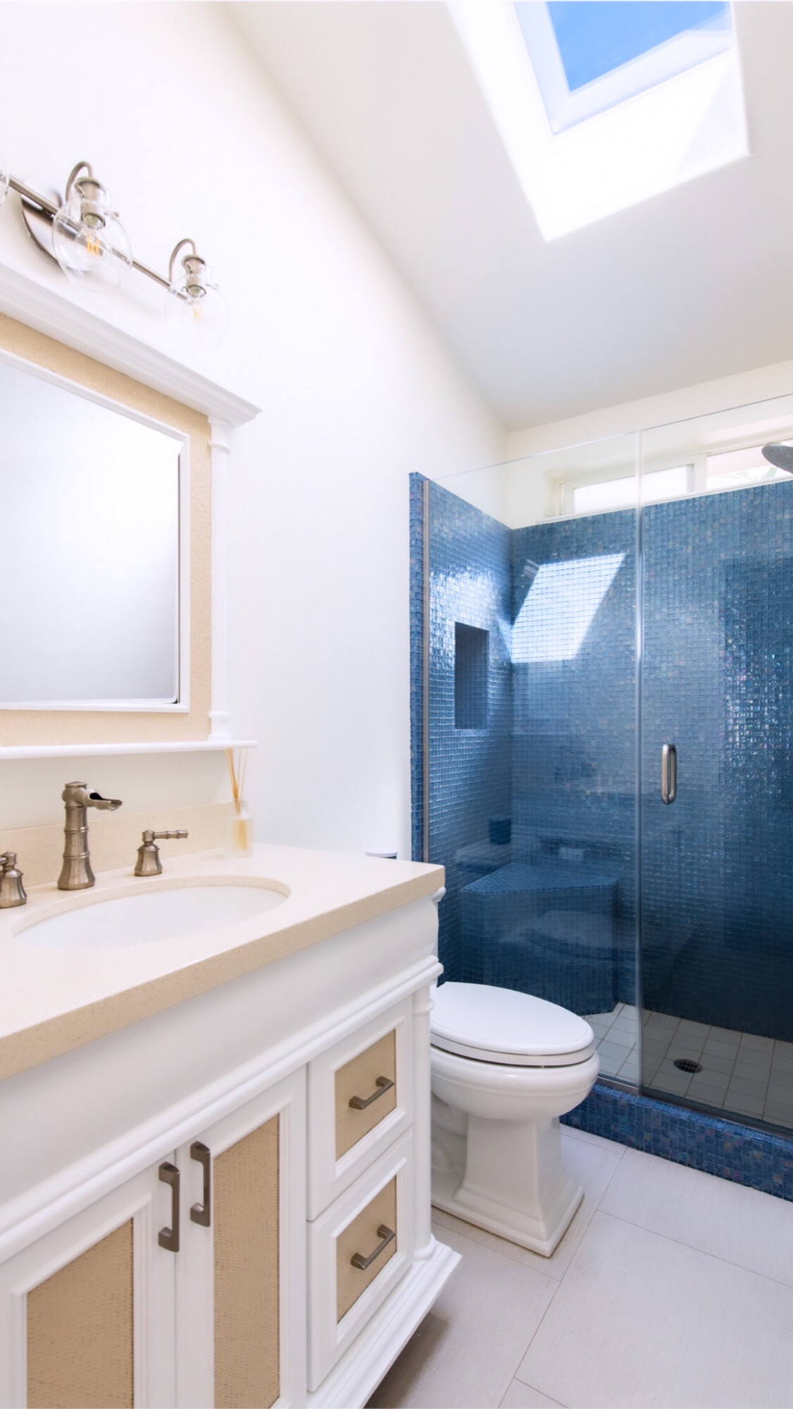 Guest bath with white and rattan vanity and blue glass tile shower.