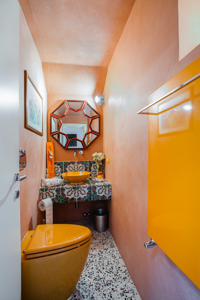 This is an example of an asian powder room in Florence with a wall-mount toilet, orange walls, mosaic tile floors, a vessel sink, tile benchtops, multi-coloured floor and multi-coloured benchtops.