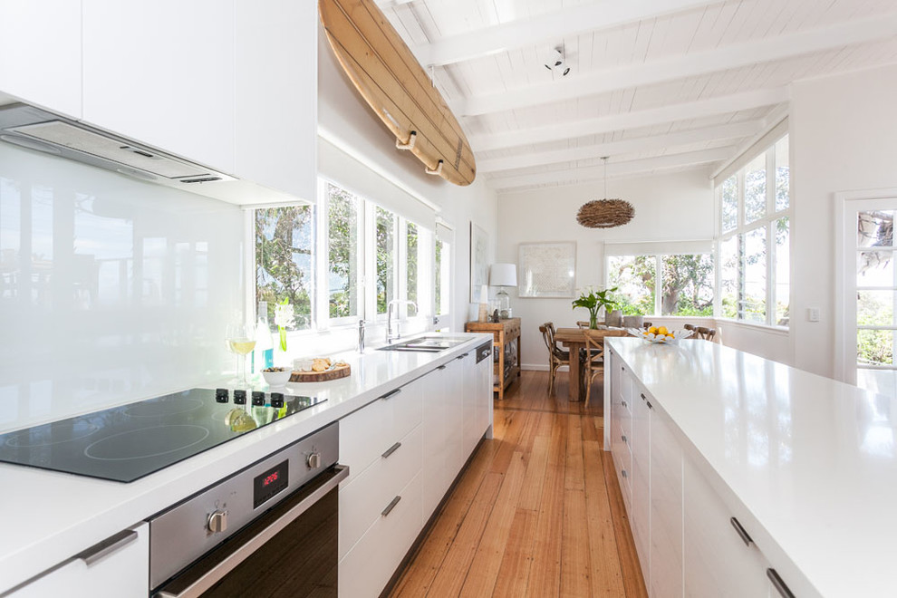 This is an example of a large modern single-wall eat-in kitchen in Cleveland with flat-panel cabinets, white cabinets, solid surface benchtops, white splashback, stainless steel appliances, medium hardwood floors, with island and brown floor.