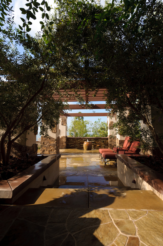 Réalisation d'une grande terrasse arrière méditerranéenne avec un point d'eau, des pavés en pierre naturelle et une extension de toiture.