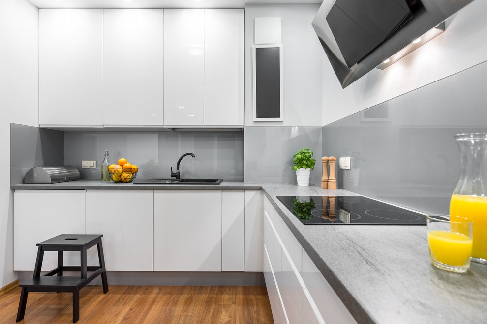 Inspiration for a mid-sized modern l-shaped kitchen in Minneapolis with a drop-in sink, flat-panel cabinets, white cabinets, concrete benchtops, grey splashback, medium hardwood floors, no island and brown floor.