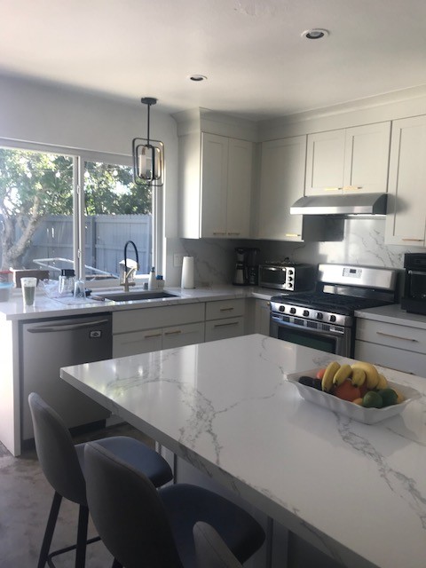 Photo of a mid-sized contemporary u-shaped eat-in kitchen in San Diego with a single-bowl sink, shaker cabinets, white cabinets, recycled glass benchtops, white splashback, cork floors, a peninsula and brown floor.