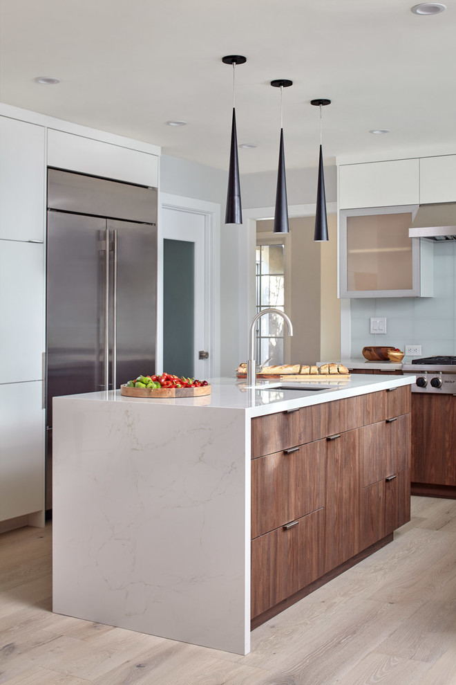 This is an example of a mid-sized modern l-shaped eat-in kitchen in San Francisco with a drop-in sink, glass-front cabinets, dark wood cabinets, quartz benchtops, green splashback, glass tile splashback, stainless steel appliances, light hardwood floors, with island, grey floor and white benchtop.