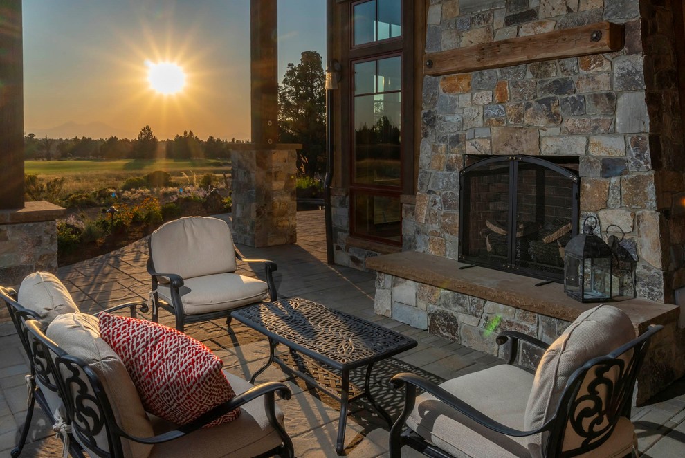 Example of a large mountain style backyard stone patio design with a fireplace and a roof extension