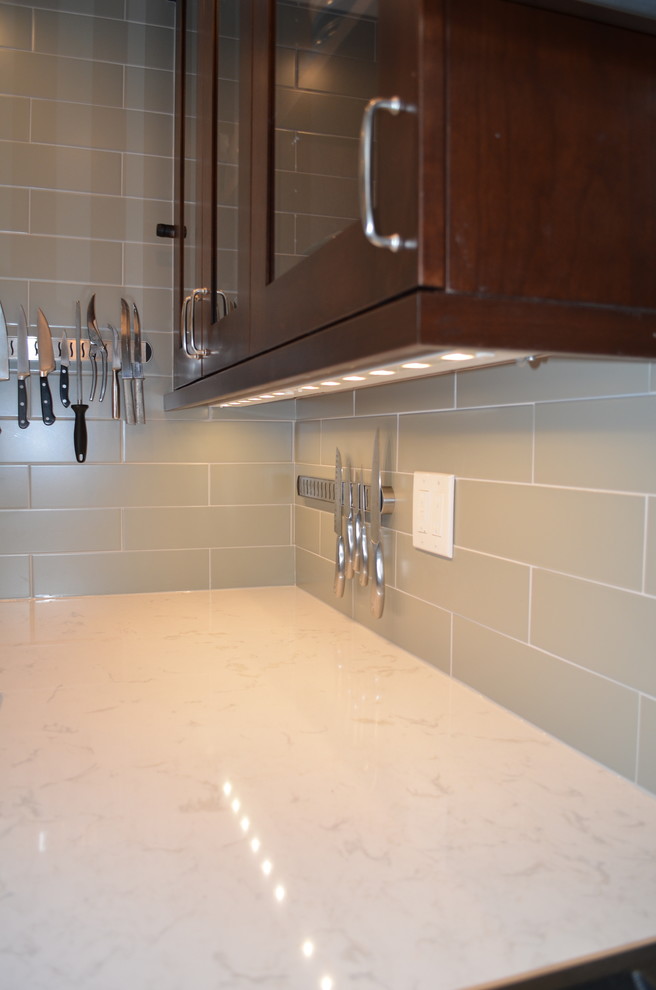 Inspiration for a mid-sized transitional l-shaped medium tone wood floor and brown floor open concept kitchen remodel in Seattle with an undermount sink, shaker cabinets, dark wood cabinets, quartz countertops, stainless steel appliances, an island, gray backsplash and subway tile backsplash