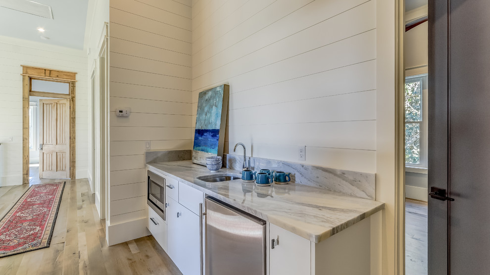 Design ideas for a small beach style single-wall wet bar in Miami with an undermount sink, flat-panel cabinets, white cabinets, marble benchtops, medium hardwood floors, brown floor and multi-coloured benchtop.