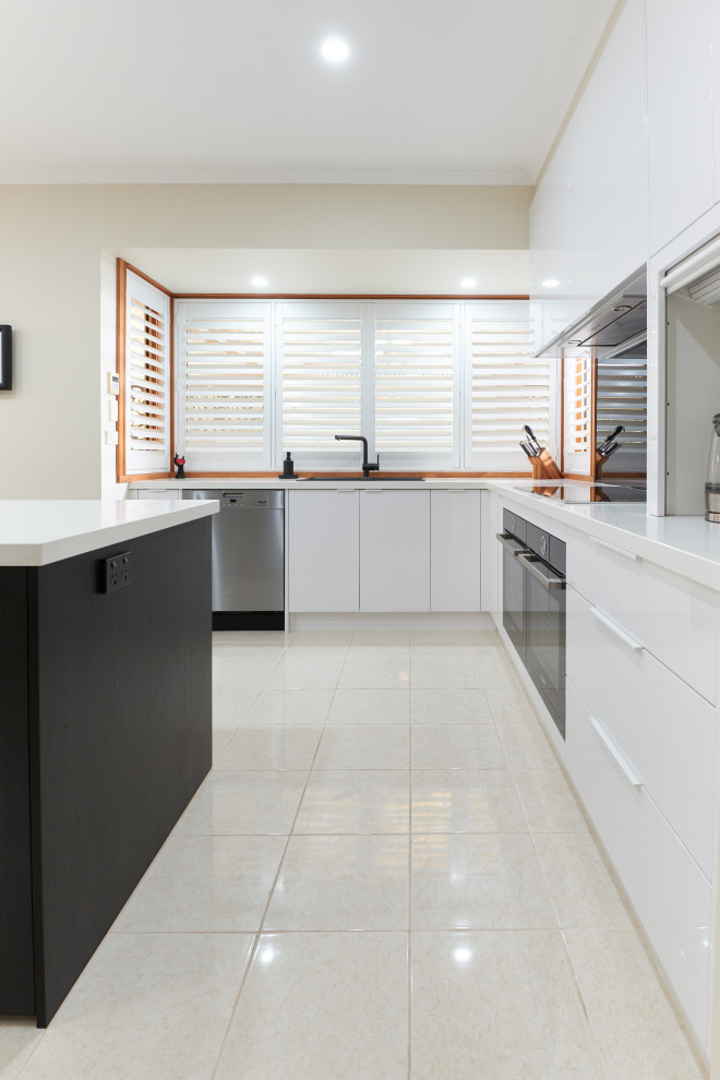Mid-sized contemporary u-shaped eat-in kitchen in Melbourne with flat-panel cabinets, white cabinets, quartz benchtops, black splashback, glass sheet splashback, black appliances, with island and grey benchtop.
