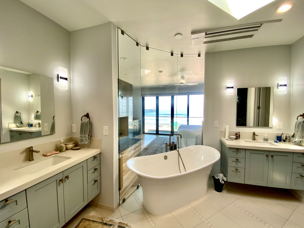 This is an example of a medium sized bohemian ensuite bathroom in San Diego with shaker cabinets, blue cabinets, a freestanding bath, a built-in shower, white tiles, glass tiles, porcelain flooring, a submerged sink, engineered stone worktops, beige floors, a hinged door, beige worktops, an enclosed toilet, double sinks and a built in vanity unit.