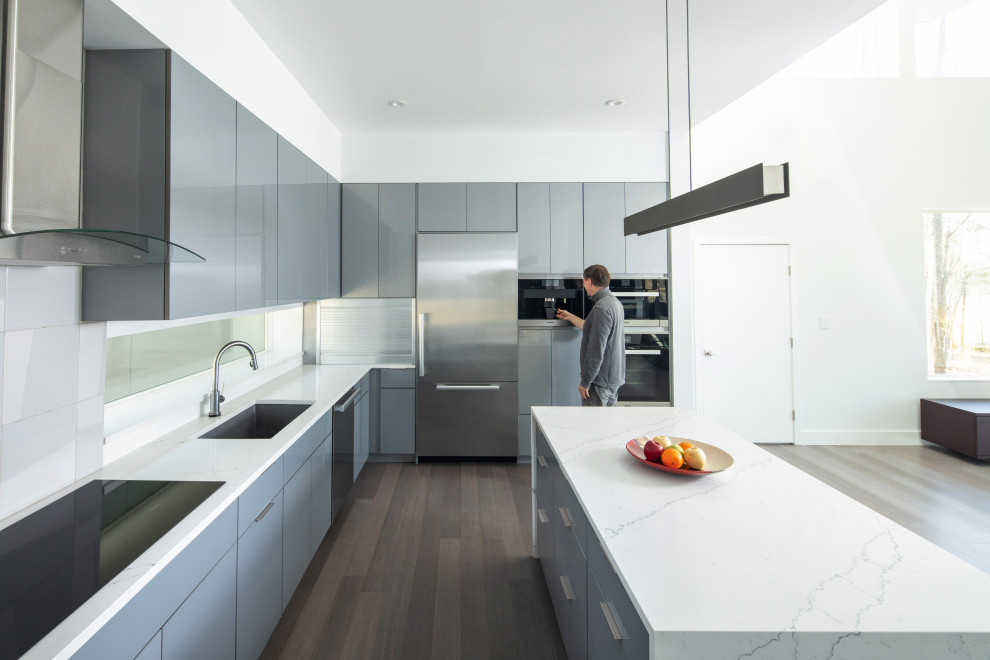 Design ideas for a medium sized modern l-shaped open plan kitchen in Raleigh with a submerged sink, flat-panel cabinets, grey cabinets, quartz worktops, grey splashback, stainless steel appliances, dark hardwood flooring, an island, brown floors and white worktops.