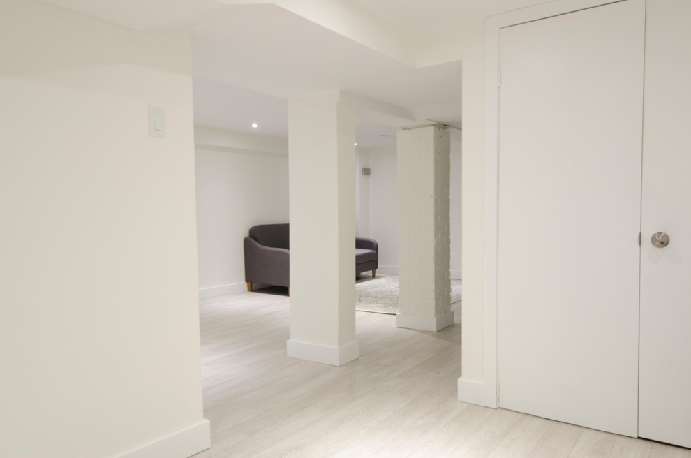 Inspiration for a mid-sized transitional look-out laminate floor and beige floor basement remodel in Toronto with white walls