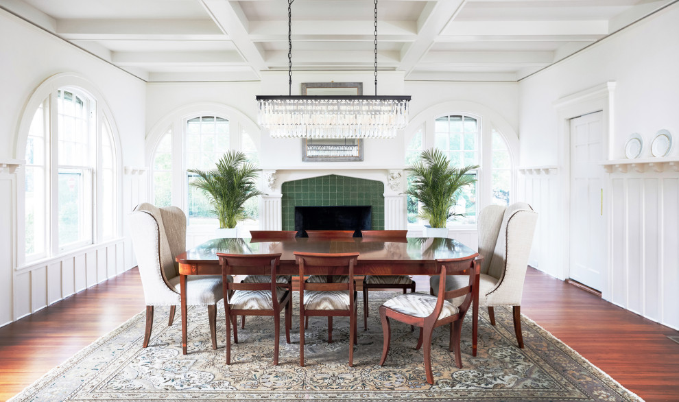 This is an example of a large classic enclosed dining room in New York with white walls, medium hardwood flooring, a standard fireplace, a tiled fireplace surround, brown floors, a coffered ceiling, wainscoting and a chimney breast.
