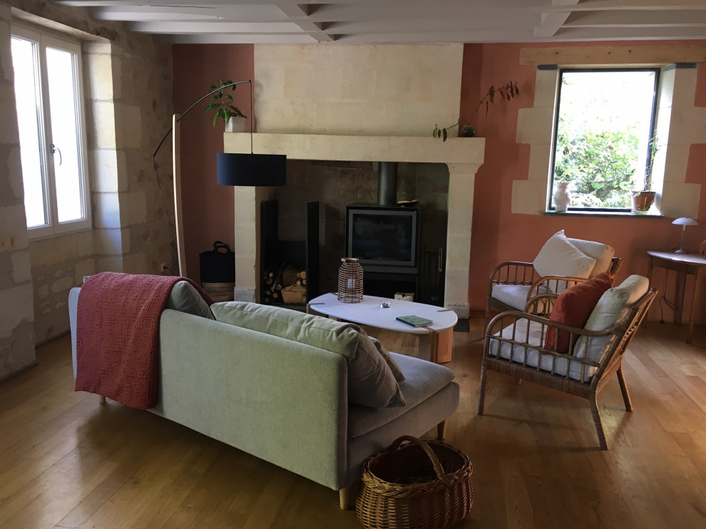 На фото: гостиная комната среднего размера в стиле кантри с розовыми стенами, светлым паркетным полом, стандартным камином, фасадом камина из камня, бежевым полом и балками на потолке