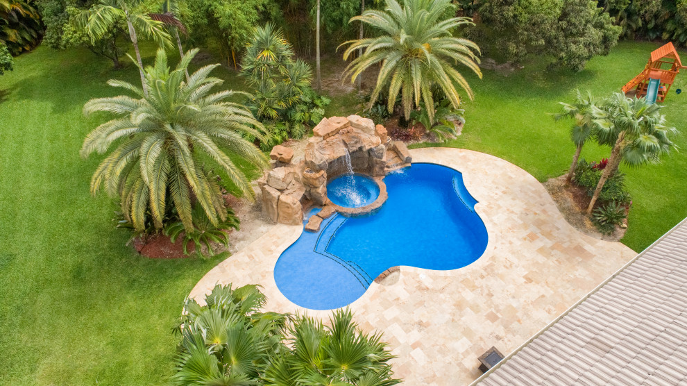 Design ideas for a large tropical backyard custom-shaped pool in Miami with a water feature and natural stone pavers.