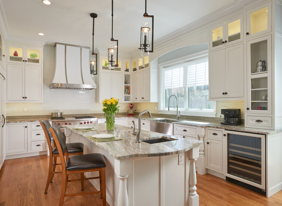 This is an example of a mid-sized transitional u-shaped eat-in kitchen in Boston with a farmhouse sink, white cabinets, white splashback, with island, shaker cabinets, marble benchtops, porcelain splashback, stainless steel appliances, light hardwood floors and brown floor.