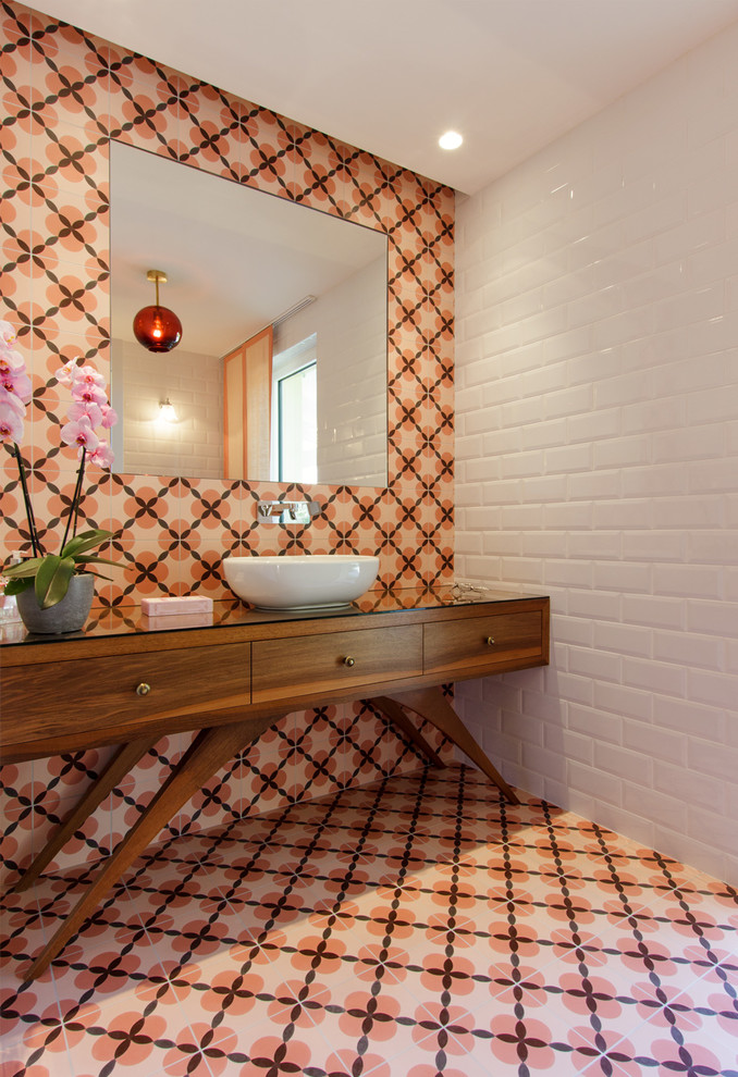 Inspiration for a midcentury powder room in Nice with furniture-like cabinets, medium wood cabinets, orange tile, white tile, mosaic tile, white walls, mosaic tile floors, a vessel sink, glass benchtops and orange floor.