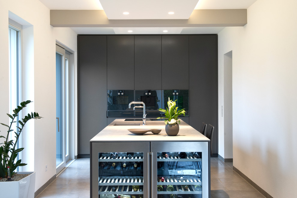 Photo of a large contemporary galley open plan kitchen in Other with an integrated sink, flat-panel cabinets, grey cabinets, stainless steel benchtops, black appliances, cement tiles, with island, beige floor and white benchtop.