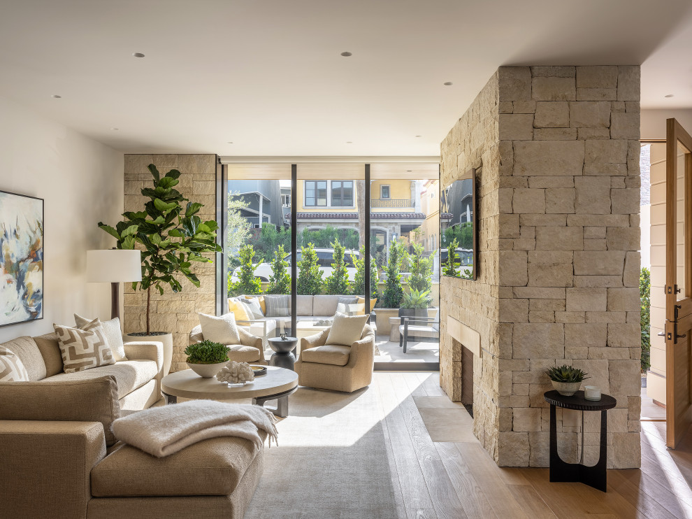 Offenes Modernes Wohnzimmer mit beiger Wandfarbe, braunem Holzboden, Kamin, Kaminumrandung aus Stein, TV-Wand und braunem Boden in Orange County