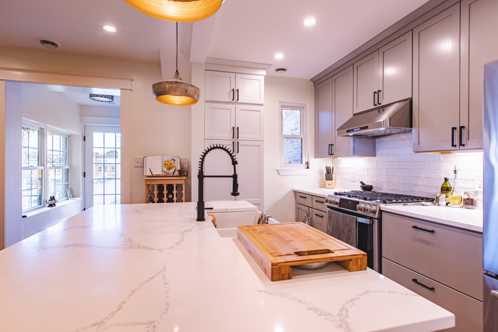 Mid-sized contemporary l-shaped open plan kitchen in DC Metro with a farmhouse sink, shaker cabinets, grey cabinets, quartzite benchtops, white splashback, subway tile splashback, stainless steel appliances, light hardwood floors, with island, brown floor and white benchtop.