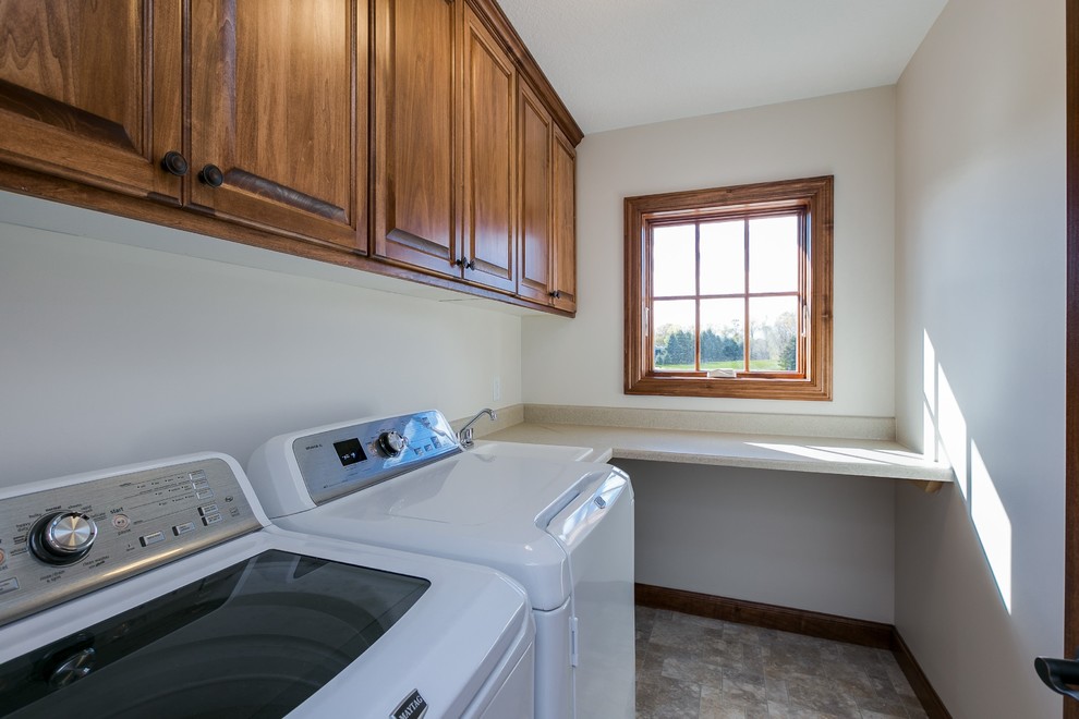 This is an example of a mid-sized traditional single-wall dedicated laundry room in Minneapolis with raised-panel cabinets, medium wood cabinets, laminate benchtops, white walls, a side-by-side washer and dryer, travertine floors and beige benchtop.