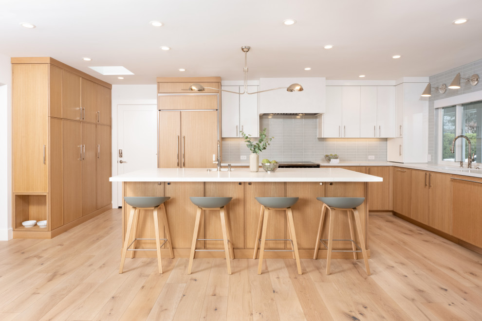 Inspiration for a large contemporary l-shaped open plan kitchen in San Francisco with a submerged sink, shaker cabinets, light wood cabinets, engineered stone countertops, green splashback, ceramic splashback, integrated appliances, light hardwood flooring, an island, brown floors and white worktops.