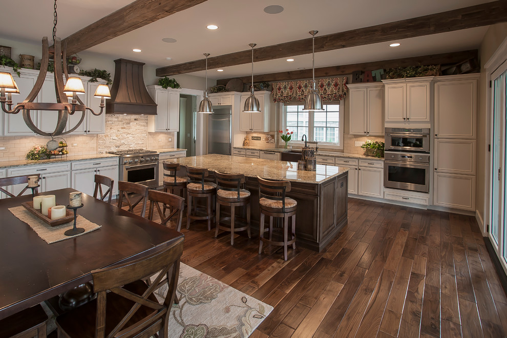 Photo of a large traditional l-shaped eat-in kitchen in Milwaukee with a farmhouse sink, raised-panel cabinets, white cabinets, granite benchtops, multi-coloured splashback, stone tile splashback, stainless steel appliances, medium hardwood floors and with island.