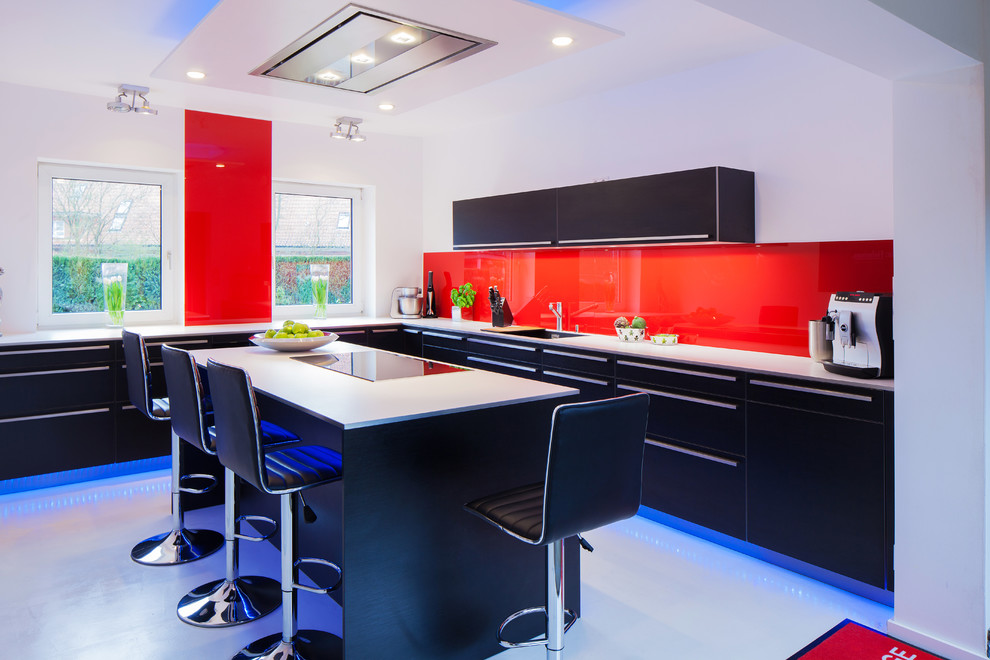 Photo of a mid-sized contemporary l-shaped open plan kitchen in Hamburg with an integrated sink, flat-panel cabinets, black cabinets, wood benchtops, red splashback, glass sheet splashback, black appliances, vinyl floors, with island and white floor.