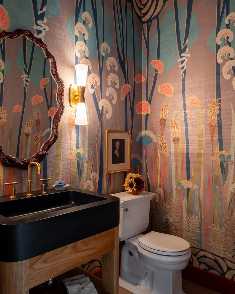Modelo de aseo de pie campestre con armarios abiertos, sanitario de dos piezas, paredes multicolor, lavabo tipo consola, encimeras negras y papel pintado