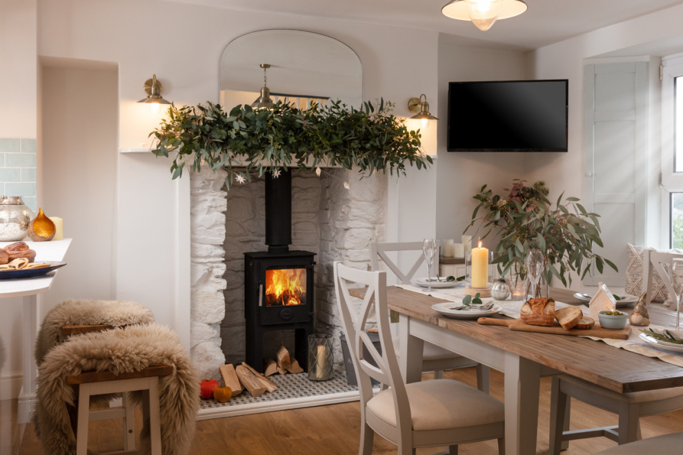 This is an example of a medium sized victorian open plan dining room in Cornwall with white walls, medium hardwood flooring, a wood burning stove, a stacked stone fireplace surround, brown floors and a chimney breast.