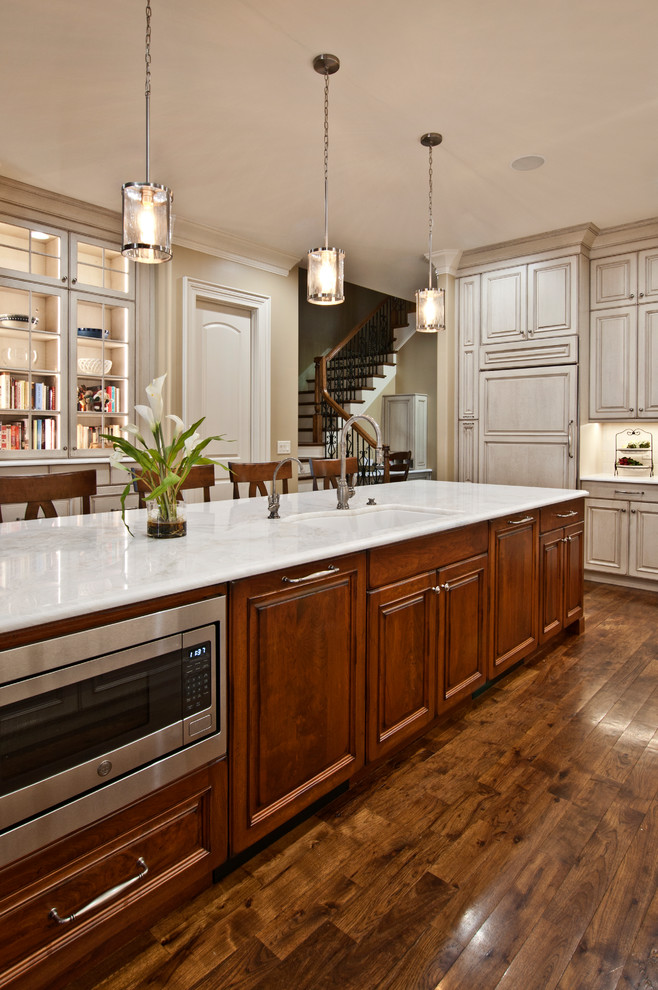 Photo of a large traditional l-shaped separate kitchen in Nashville with an undermount sink, raised-panel cabinets, beige cabinets, marble benchtops, beige splashback, ceramic splashback, panelled appliances, medium hardwood floors, with island, brown floor and white benchtop.