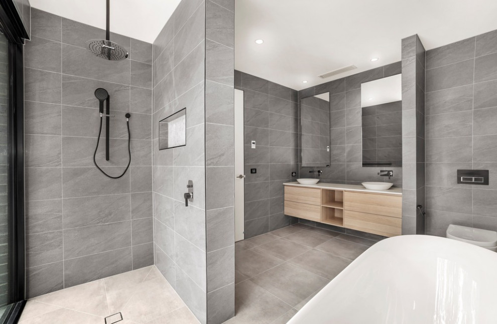 This is an example of a modern master bathroom in Melbourne with flat-panel cabinets, light wood cabinets, a freestanding tub, an open shower, a wall-mount toilet, gray tile, porcelain tile, grey walls, porcelain floors, a vessel sink, quartzite benchtops, grey floor, an open shower, white benchtops, a double vanity and a floating vanity.