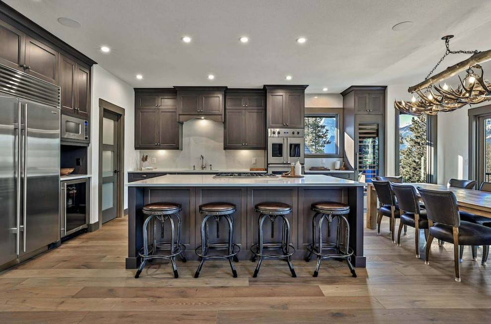 Design ideas for an expansive traditional l-shaped open plan kitchen in Calgary with an undermount sink, shaker cabinets, dark wood cabinets, quartz benchtops, grey splashback, limestone splashback, stainless steel appliances, medium hardwood floors, with island, brown floor and grey benchtop.