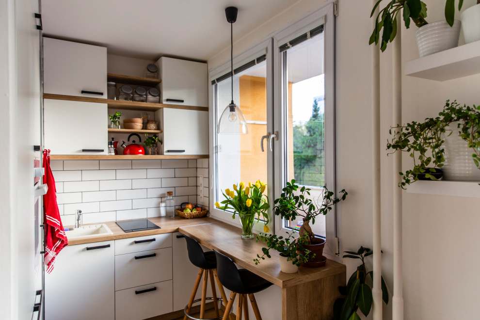 This is an example of a small contemporary l-shaped eat-in kitchen in Other with a drop-in sink, flat-panel cabinets, white cabinets, laminate benchtops, white splashback, ceramic splashback, black appliances, bamboo floors, with island, brown floor and brown benchtop.