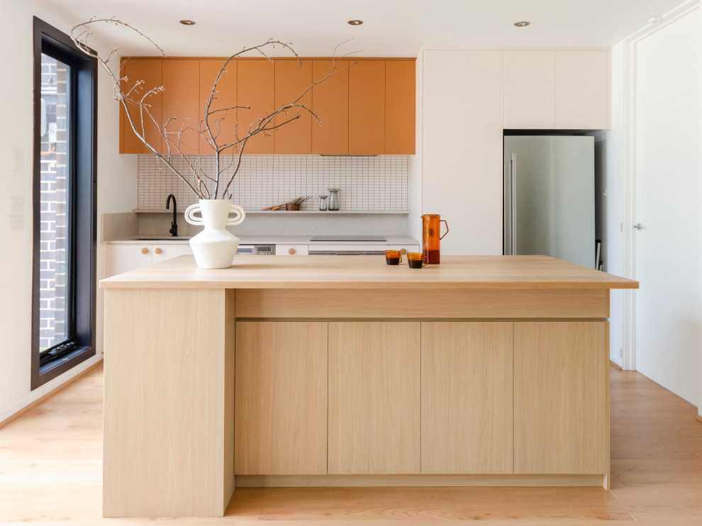 Design ideas for a medium sized contemporary galley kitchen in Melbourne with a submerged sink, flat-panel cabinets, orange cabinets, wood worktops, white splashback, mosaic tiled splashback, stainless steel appliances, laminate floors, an island, beige floors and beige worktops.