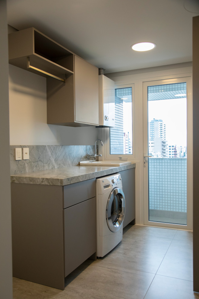 Mid-sized contemporary single-wall dedicated laundry room in Melbourne with an utility sink, flat-panel cabinets, grey cabinets, beige walls, porcelain floors, a stacked washer and dryer, beige floor, grey benchtop and marble benchtops.