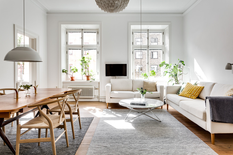 This is an example of a scandinavian open concept family room in Stockholm with white walls, medium hardwood floors, a wall-mounted tv and brown floor.