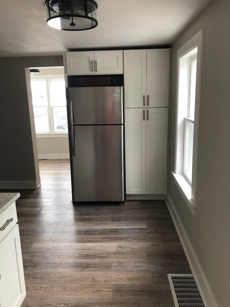 Photo of a small country l-shaped separate kitchen in Milwaukee with an undermount sink, shaker cabinets, white cabinets, granite benchtops, white splashback, ceramic splashback, stainless steel appliances, vinyl floors, no island, brown floor and white benchtop.