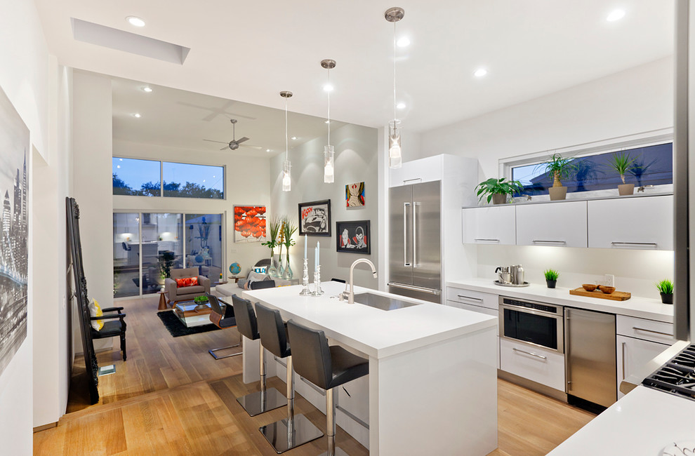 Photo of a modern l-shaped open plan kitchen in Los Angeles with an undermount sink, flat-panel cabinets, white cabinets, white splashback and stainless steel appliances.